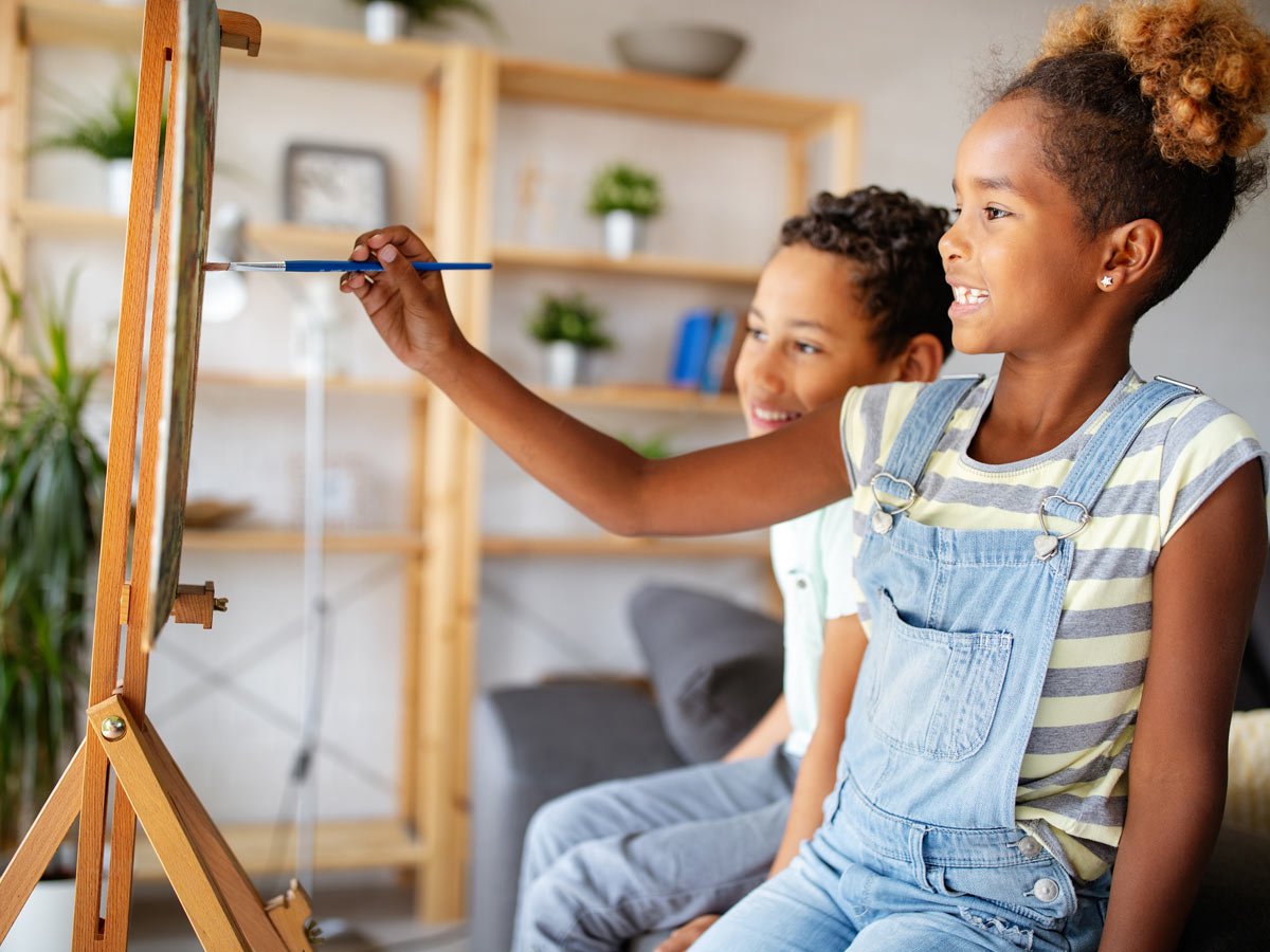 Niños pintan en un bastidor con pincel en un atril